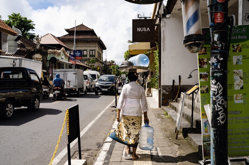 Balinese woman carrying water jug on head along street