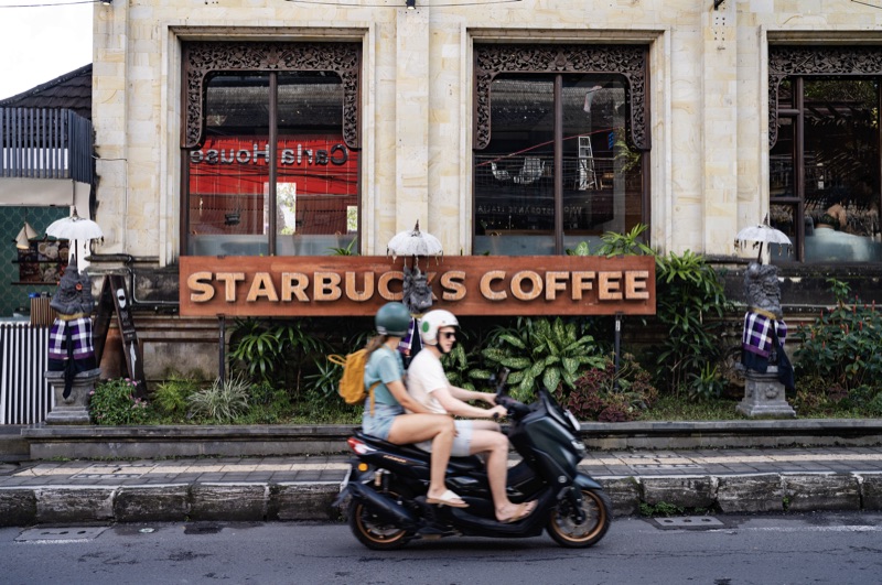Couple on scooter passing Balinese Starbucks